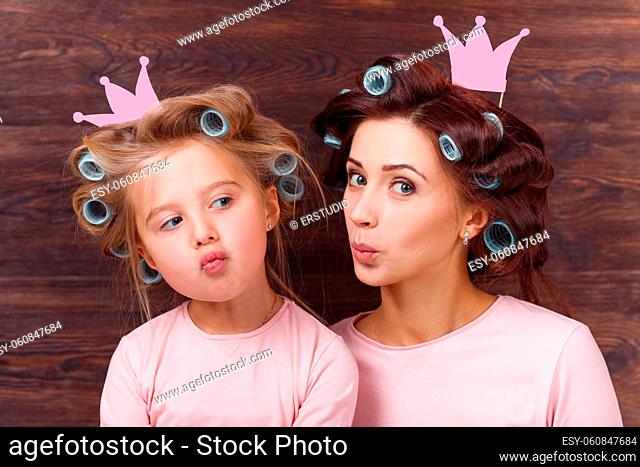 young mother and daughter with hair curlers having fun together and holding paper crown