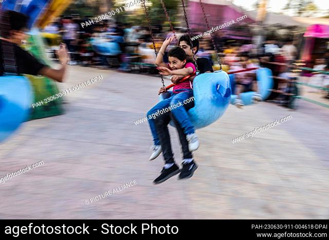 29 June 2023, Syria, Idlib: Syrian children ride on a swing carousel at the City Park during the celebrations of the Eid al-Adha holiday in Idlib