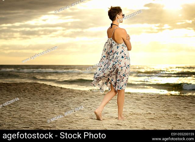 beautiful woman in a long dress is walking on the beach at sunset