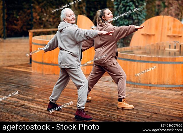 Young and elderly woman warming up and yoga exercises outdoor. Grandmother and granddaughter having zen like modern fitness vacation