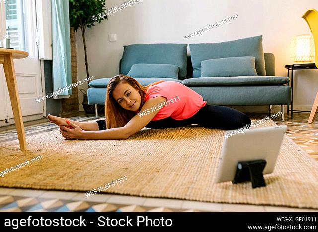 Young woman looking at digital tablet while practicing exercise at home