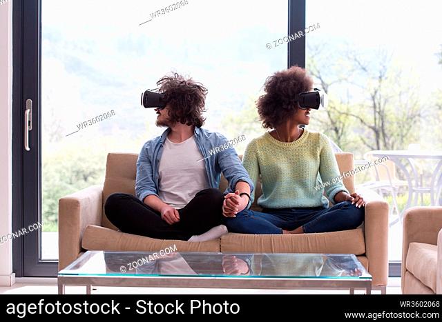 Multiethnic Couple using virtual reality headset in living room at home people playing game with new trends technology