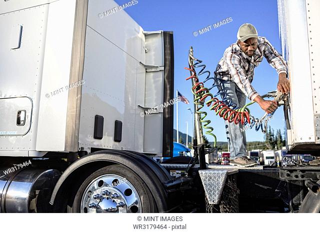Black man truck driver attaching power cables from truck tractor to trailer at a truck stop