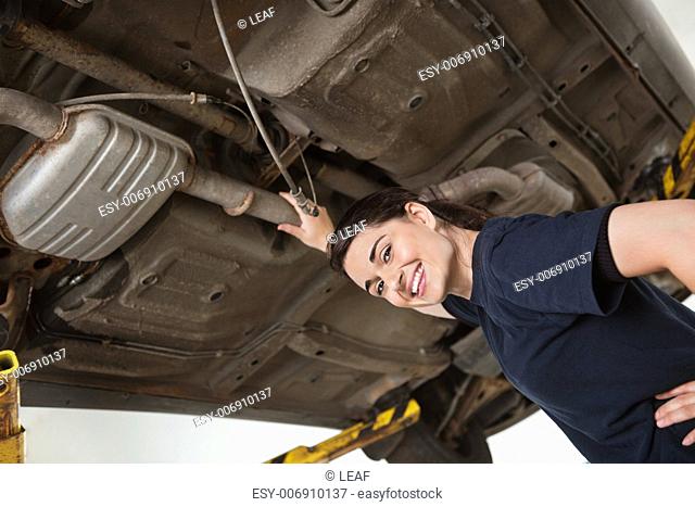 Low angle view of smiling young female mechanic repairing car in auto repair shop