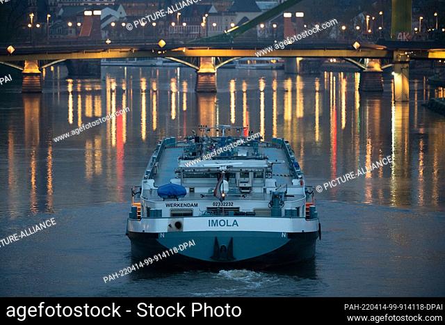 14 April 2022, Hessen, Frankfurt/Main: A barge sails on the Main River in the city center in the early morning, with the lights of the skyline and those of a...