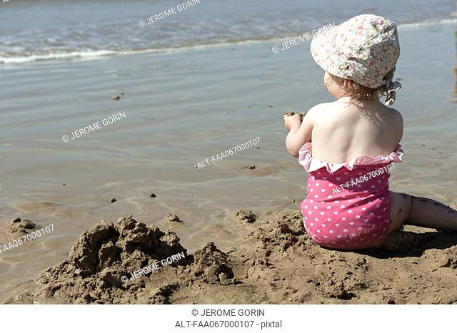 Toddler girl playing in sand at the beach, rear view