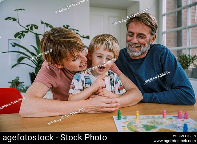 Mother embracing son while father sitting beside playing board game at home