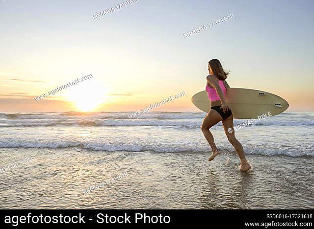 Young woman entering onshore waves holding surfboard in early morning