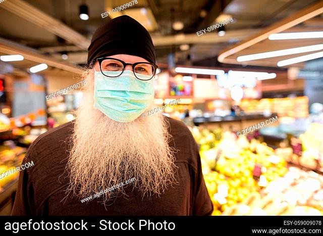 Portrait of mature bearded hipster man with mask for protection from corona virus outbreak social distancing at the supermarket