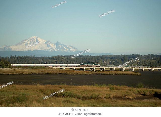 Amtrak Cascades train passing Mud Bay with Mount Baker in Surrey, BC, Canada