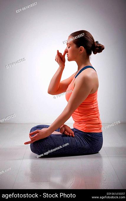 Beautiful sporty fit yogini woman practices pranayama breath control exercise in yoga asana Padmasana - lotus pose with Vishnu mudra in studio