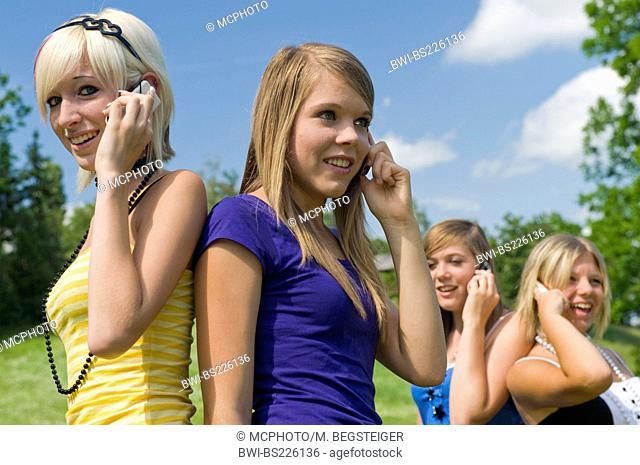 four young girls standing in a meadow phoning with a mobile with a smile