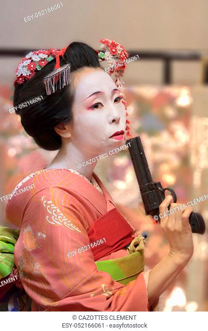 Pretty young Geisha maiko girl in kimono holding a plastic gun in her hand