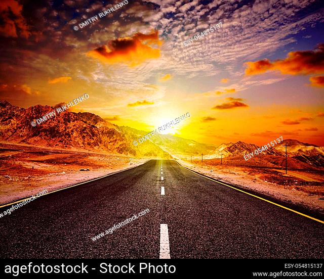 Travel forward concept background - vintage retro effect filtered hipster style image of road in Himalayas with mountains and dramatic clouds on sunset
