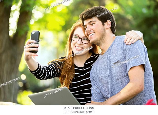 A young man and young woman taking a self-portrait on a smart phone; Edmonton, Alberta, Canada