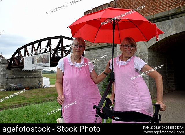25 August 2023, Lower Saxony, Langendorf: Twin sisters Uta (l) and Edda Heidenblut from Eldena stand in front of the historic Dömitzer railroad bridge on the...
