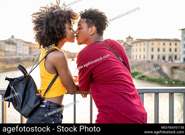 Young tourist couple kissing on a bridge above river Arno at sunset, Florence, Italy