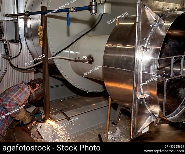 Tradesman grinding a weld for a heating package in a fabrication plant; Innisfail, Alberta, Canada