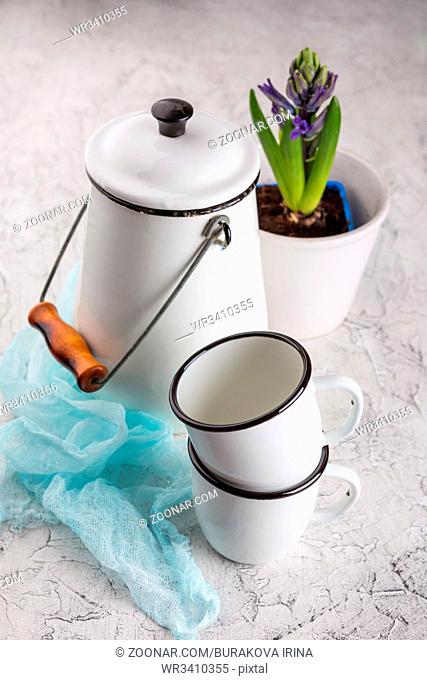 Two white enamel mugs, white can and blossoming flower hyacinth in pot on light background