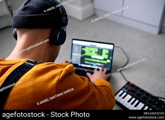 Freelancer wearing wireless headphones using laptop by piano at home studio