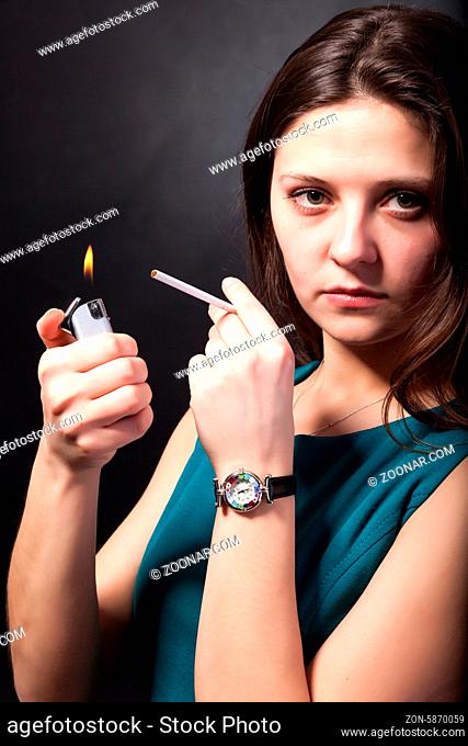 Beautiful young woman is smoking cigarette on black background