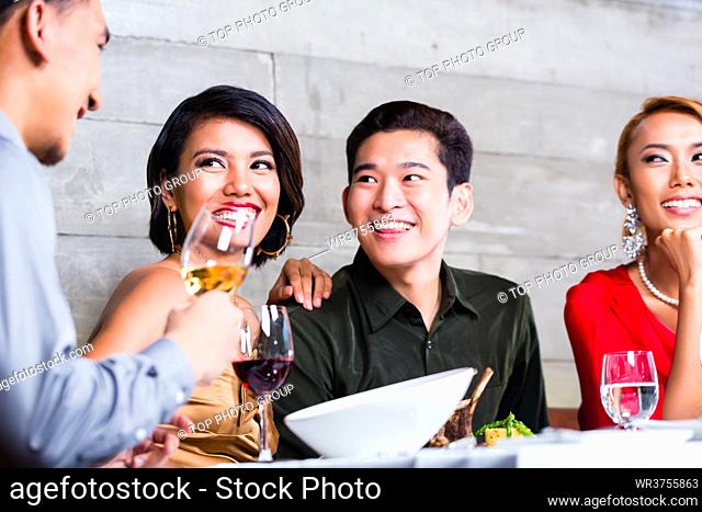 Asian friends, two couples, dining in fancy restaurant eating good food and drinking wine