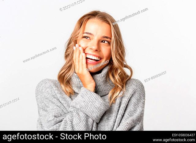 Close-up of attractive happy woman in grey sweater, smiling and looking pleased at upper left corner logo, standing over white background