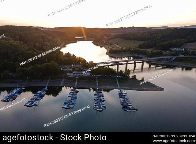 12 September 2020, North Rhine-Westphalia, Attendorn-Wamge: The sun sets on Lake Bigge behind a sailing harbour and a bridge