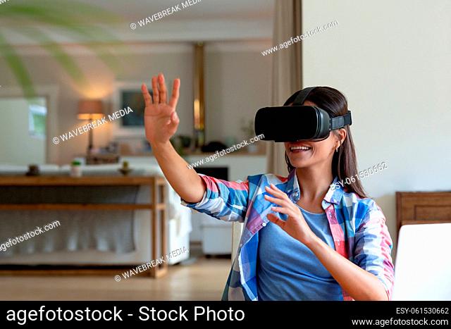 Caucasian woman sitting by desk using a vr headset and smiling