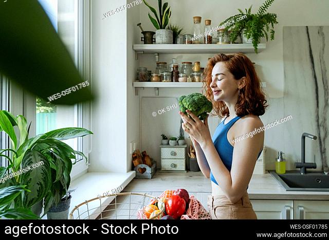 Smiling young woman smelling broccoli in kitchen at home