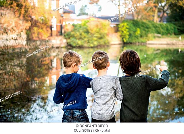 Three young boys, standing beside lake, rear view