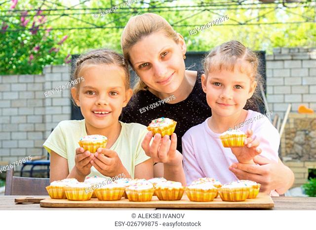 Mother and two daughters sitting at the table with Easter cupcakes in his hands and looked into the frame