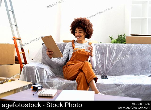 Smiling woman holding checklist on clipboard in new home