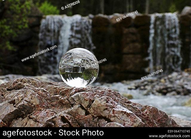 A glass sphere reflects a waterfall in the mountains