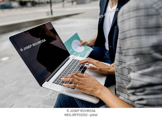 Close-up of two colleagues working together on laptop outdoors