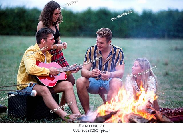 Young man playing guitar at bonfire party in park