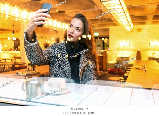 Young woman taking selfie with smartphone in cafe, London, UK