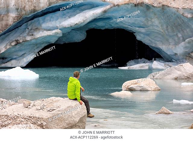 Hiker looking at an ice cave at the toe of the Dartmouth Glacier, BC, Canada