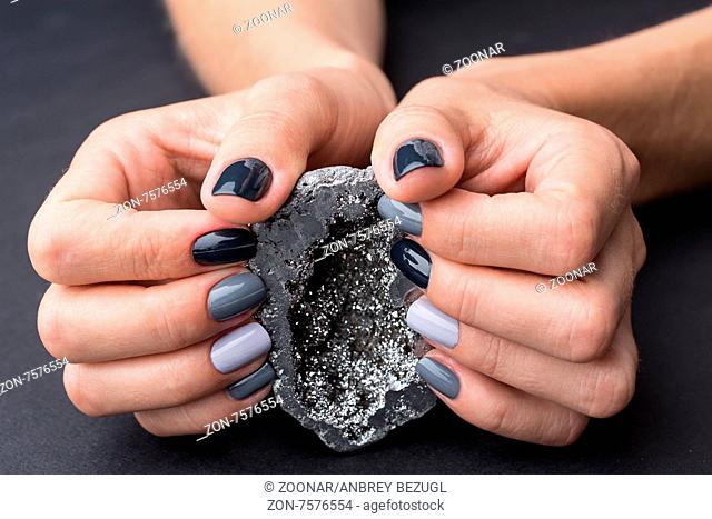 Well-groomed female hands with a stylish manicure holding a beautiful textured silver mineral. Nail painted gray paint different tonality