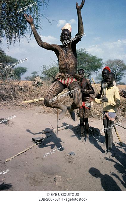 Dinka tribesman with his body painted with ash leaping in to air with his arms held in the shape of the horns of a bull during dance