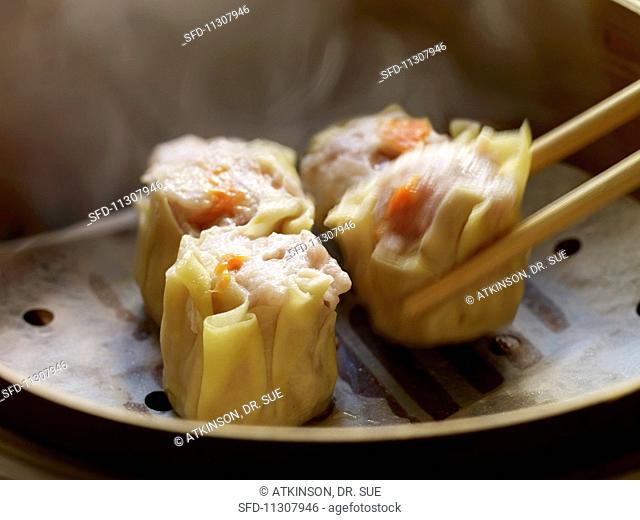 Siu Mai Dim Sum (Cantonese pork and prawn dumplings) one being lifted with chop sticks