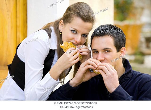 Young couple eating sandwiches on the street