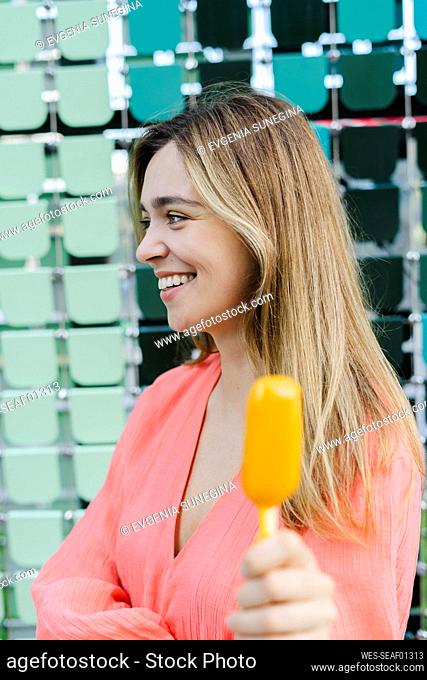 Happy woman showing ice cream in front of glass wall