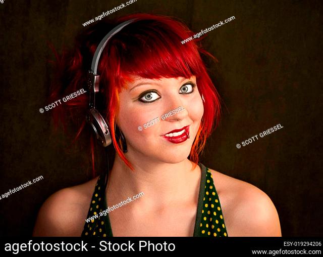 Pretty punky girl with brightly dyed red hair listening to music