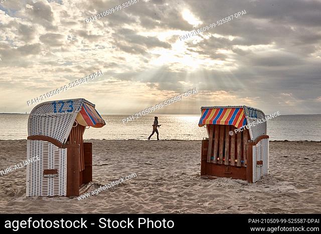 dpatop - 09 May 2021, Schleswig-Holstein, Scharbeutz: A woman jogs along the beach. In the foreground two beach chairs can be seen