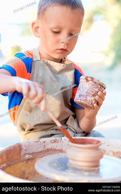 Hands of young potter, creating an earthen jar on the circle, close-up. Little smiling boy produced on potters wheel pot