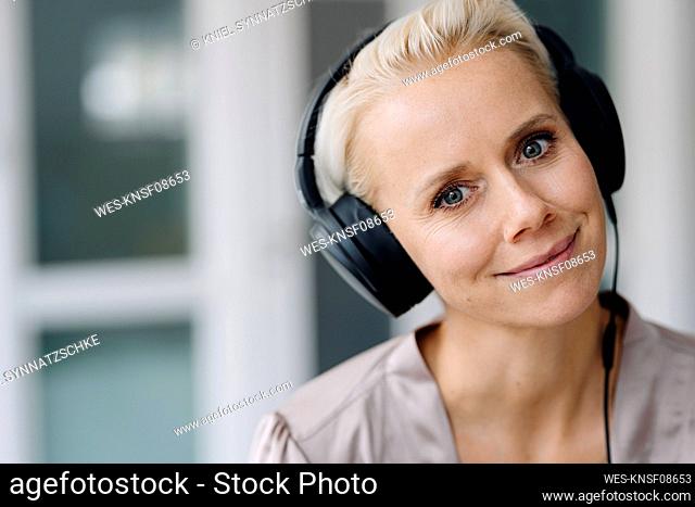 Close-up of smiling businesswoman listening music over headphones in office