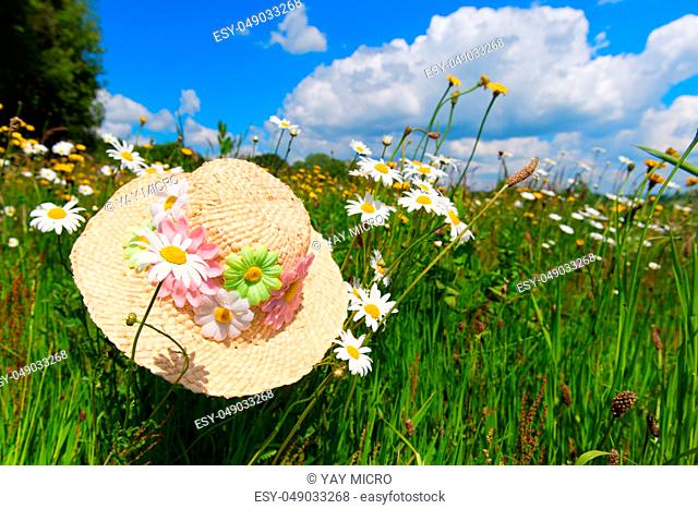 Straw summer hat with flowers in flower field with daisies and yellow butter cups