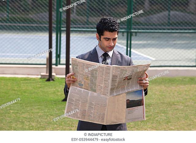 Young male corporate business executive reading newspaper in a tennis court