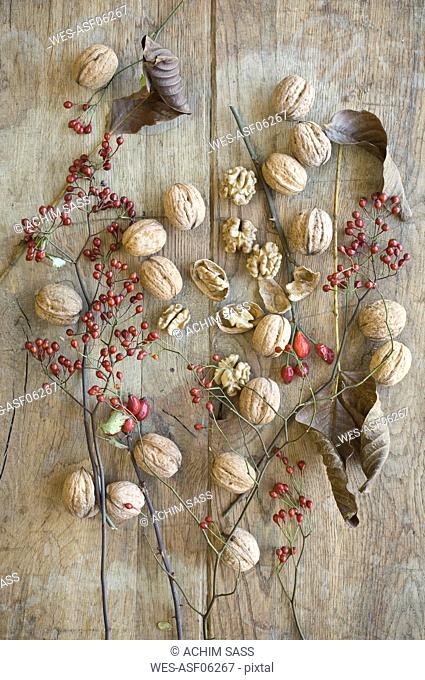 Whole and cracked organic walnuts, leaves and roseships on wood